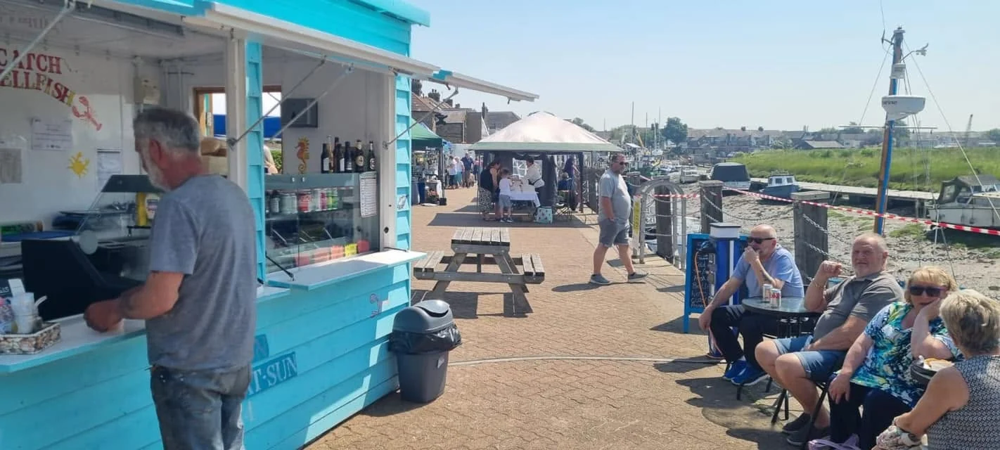 Customers enjoying food and drinks beside The Little Blue Hut and Queenborough harbour